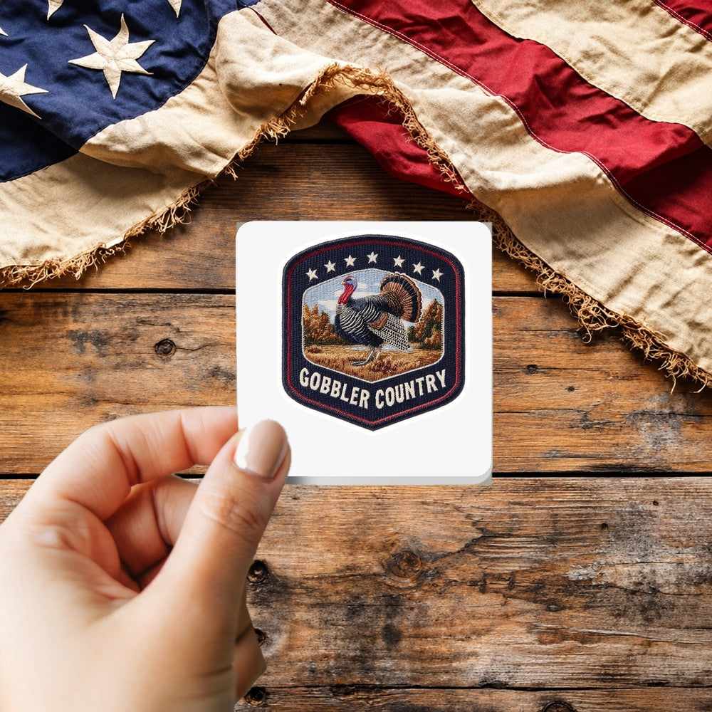 Gobbler Country sticker held over a vintage American flag on rustic wood, patriotic Thanksgiving gift