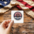 Grateful Nation sticker held over a vintage American flag on rustic wood, patriotic Thanksgiving gift