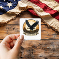 Harvest Home Eagle sticker held over a vintage American flag on rustic wood, patriotic Thanksgiving gift