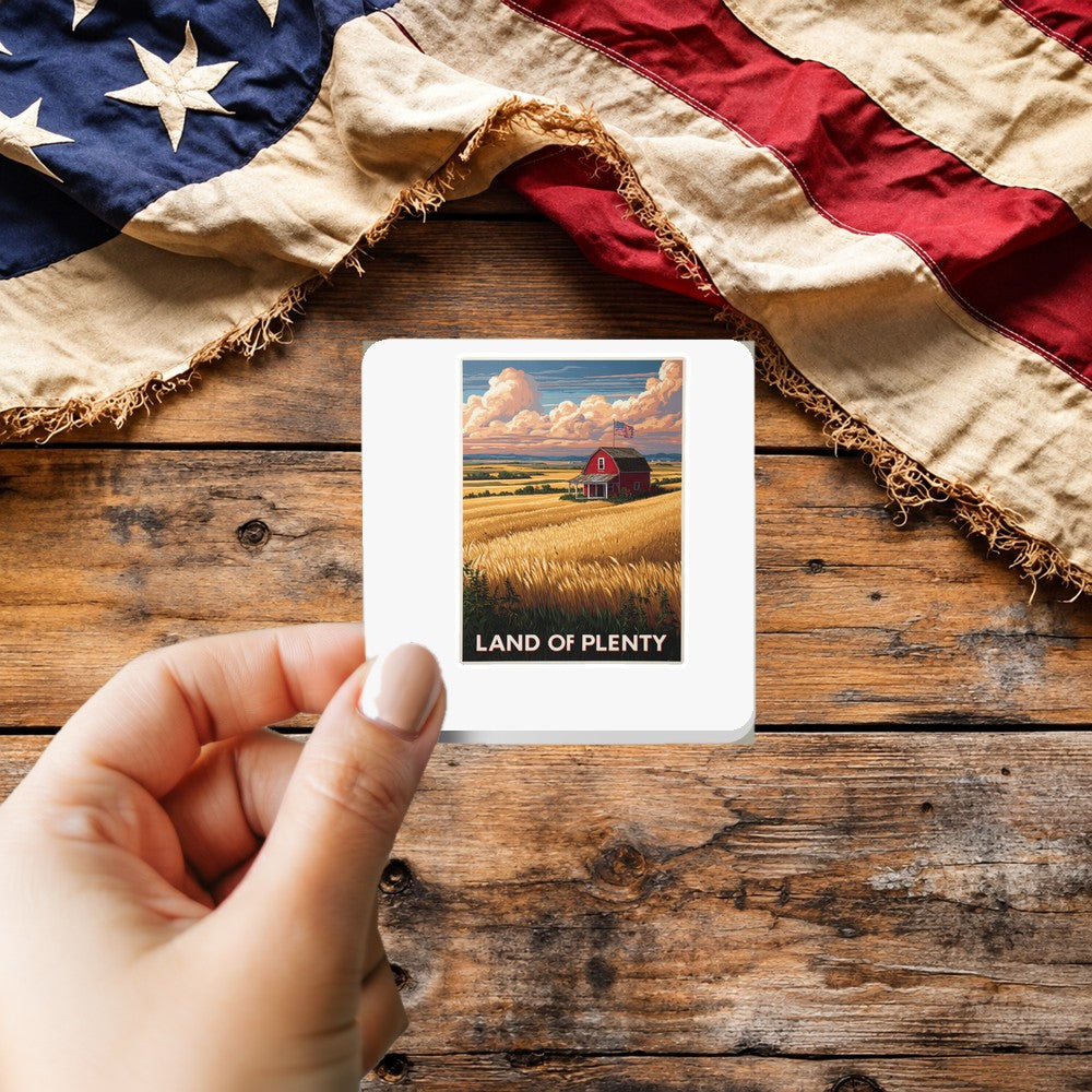 Land of Plenty sticker held over a vintage American flag on rustic wood, patriotic Thanksgiving gift