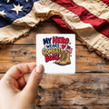 My Hero Wears Combat Boots sticker held over a vintage American flag on rustic wood, Veterans Day gift