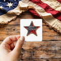Proud American Veteran Enamel Pin Style sticker held over a vintage American flag on rustic wood, Veterans Day gift
