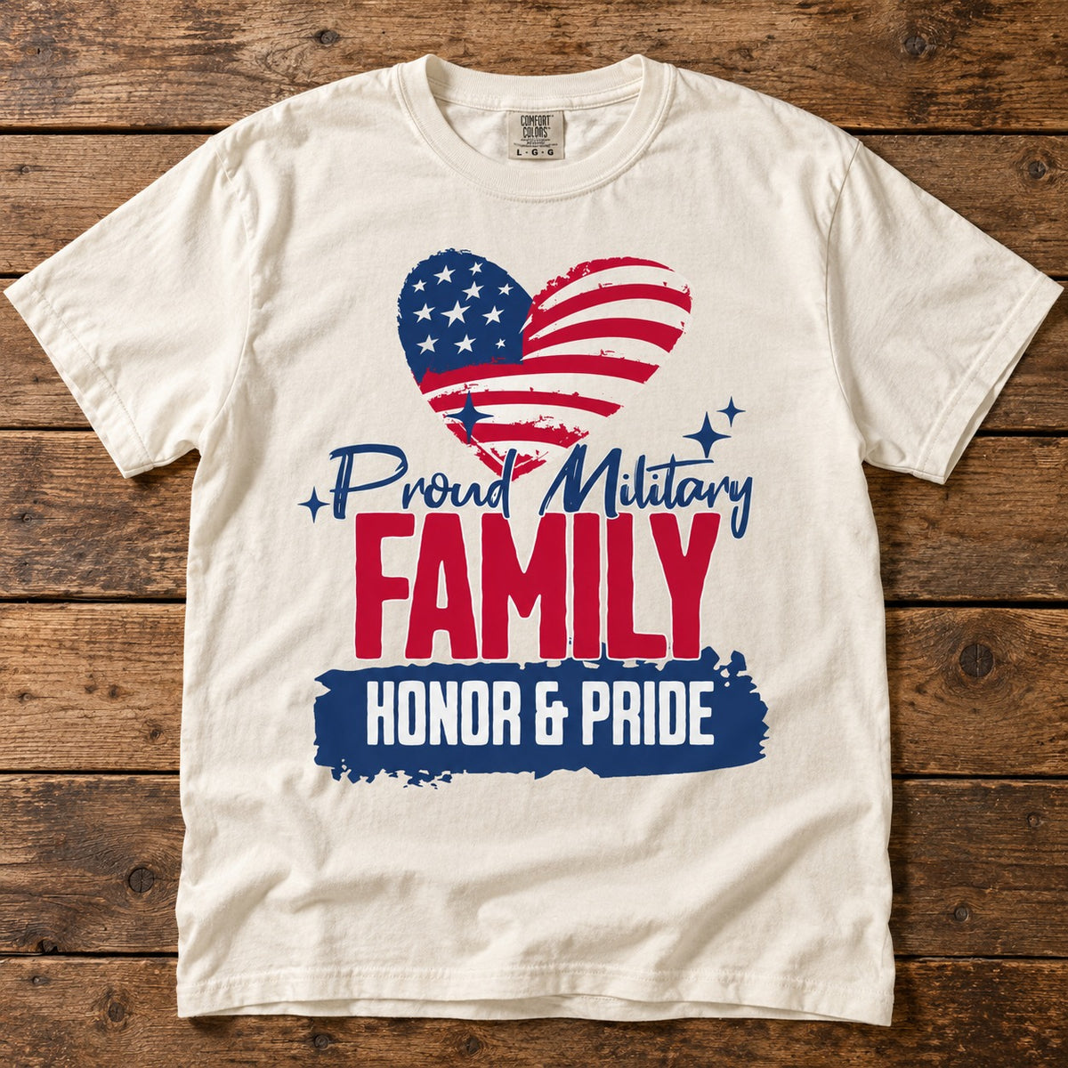 Proud Military Family shirt with an American flag heart, Proud Military script, red FAMILY lettering and HONOR & PRIDE banner, on an ivory tee laid on wood