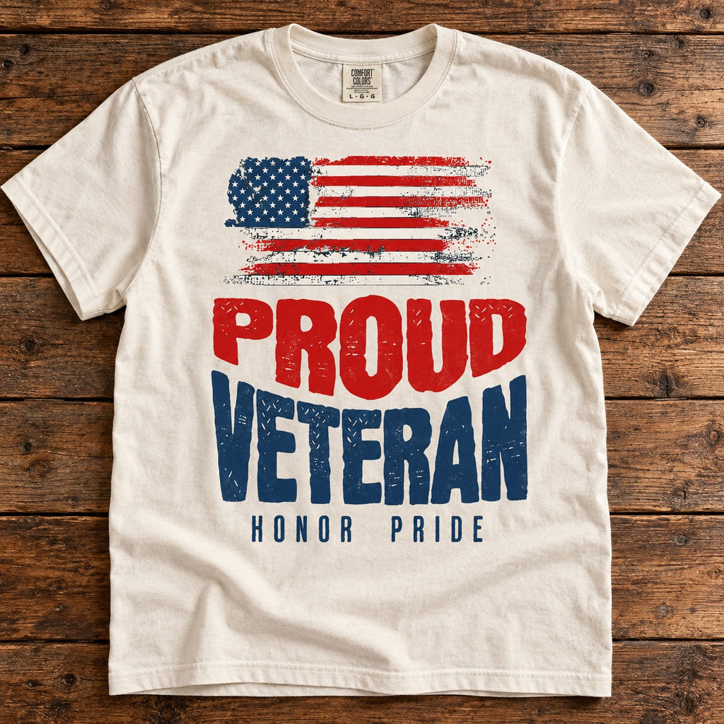 Proud Veteran shirt with a distressed American flag above red and navy PROUD VETERAN lettering and HONOR PRIDE, on an ivory tee laid on wood