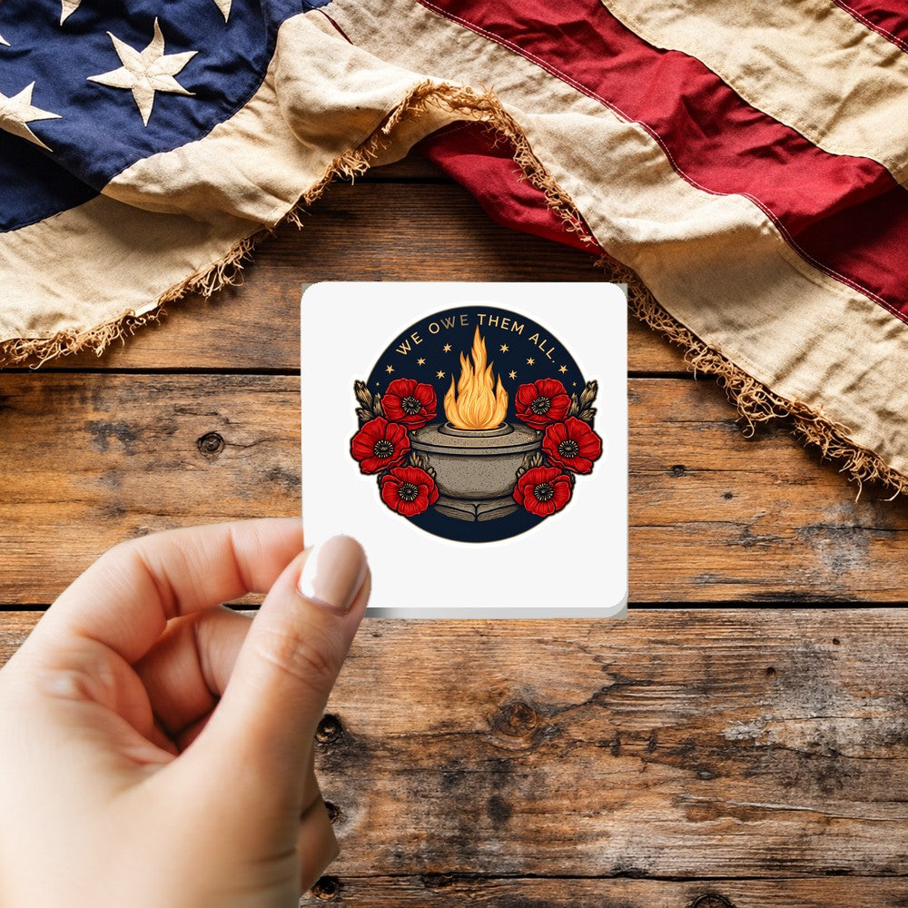We Owe Them All sticker held over a vintage American flag on rustic wood, Veterans Day gift